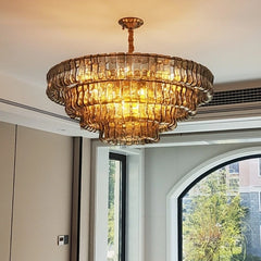 A close-up view of a multi-tiered gold chandelier with amber glass accents, illuminated against a white ceiling.