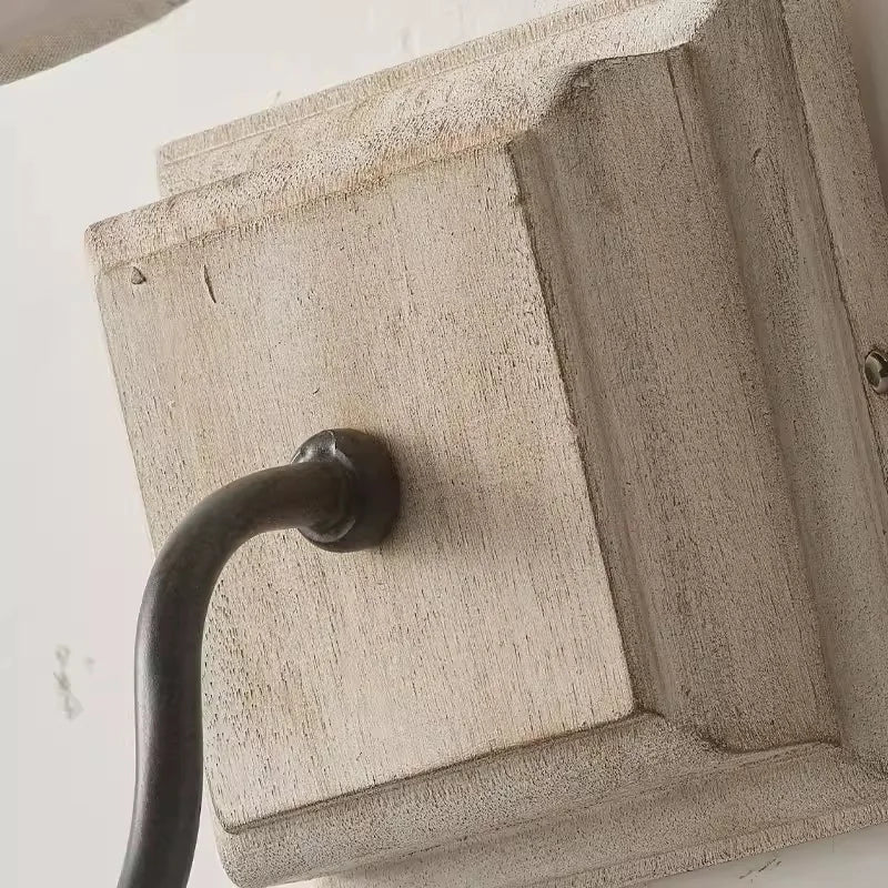 Close-up view of the distressed white wood backplate of a wall sconce, showing texture and the point where a dark metal arm attaches.