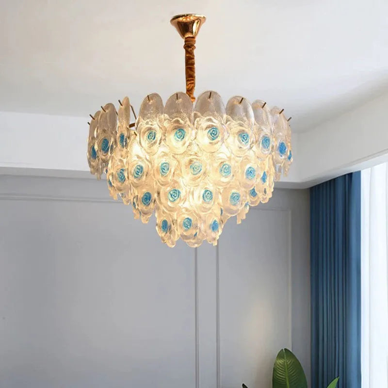Brushed gold chandelier with clear glass and blue rose accents, shown in a living room setting.