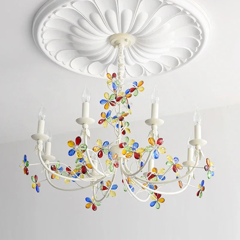Angled view of a white chandelier with colorful crystal floral details and candle-style bulbs illuminating a room.