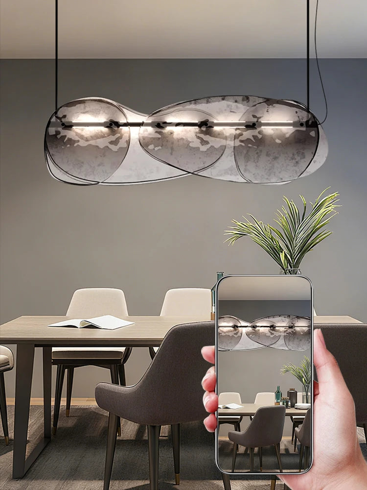Modern dining room with a pendant light and a hand holding a phone taking a photo.
