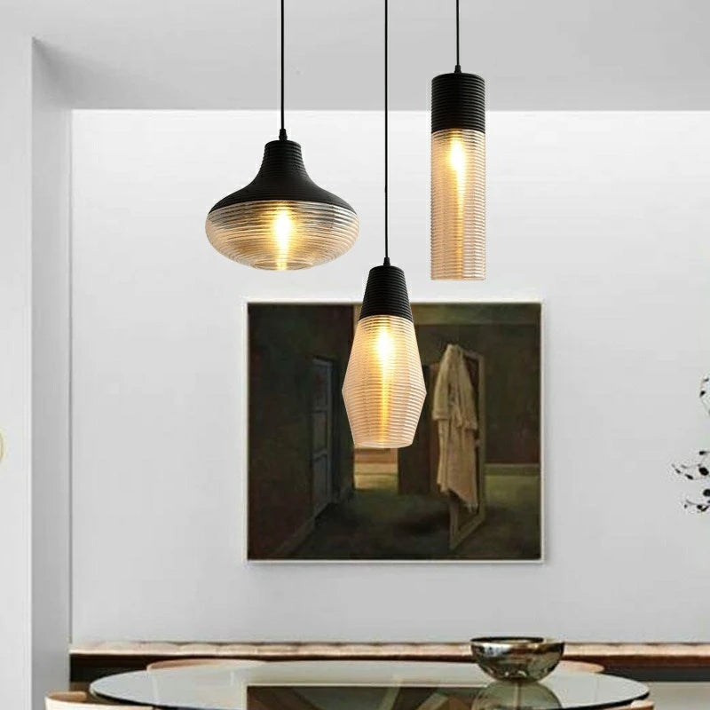 A group of three pendant lights with ribbed glass shades, one featuring a large painting in the background.