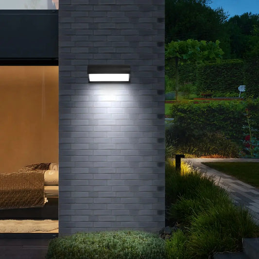 Close-up of a modern black LED wall sconce attached to a grey brick wall, casting bright light downwards.