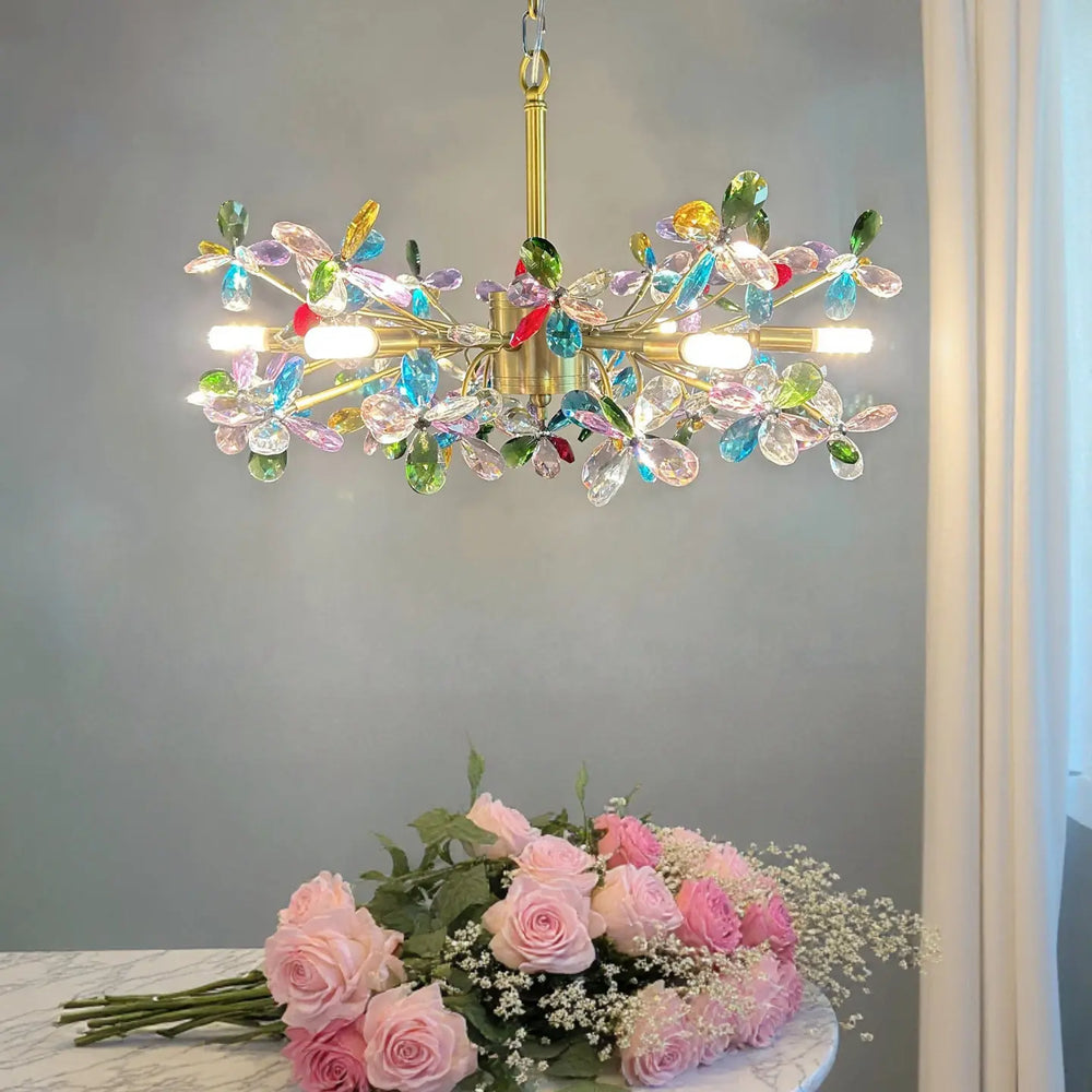 A gold chandelier with colorful crystal flowers, shown above a bouquet of pink roses.