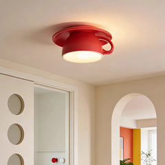 A close-up of a red ceramic coffee cup shaped ceiling light with a saucer-like base.