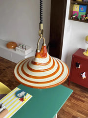 Orange and white striped horn-shaped pendant light hanging over a green table in a brightly decorated room.