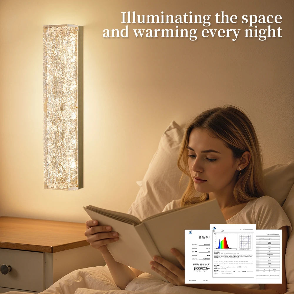 Woman reading a book in bed with a wall sconce illuminating the space.