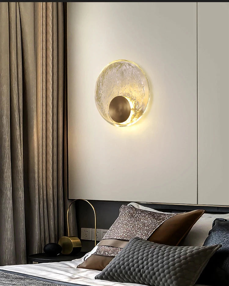 Modern wall lamp above a bed with decorative pillows in a bedroom setting.