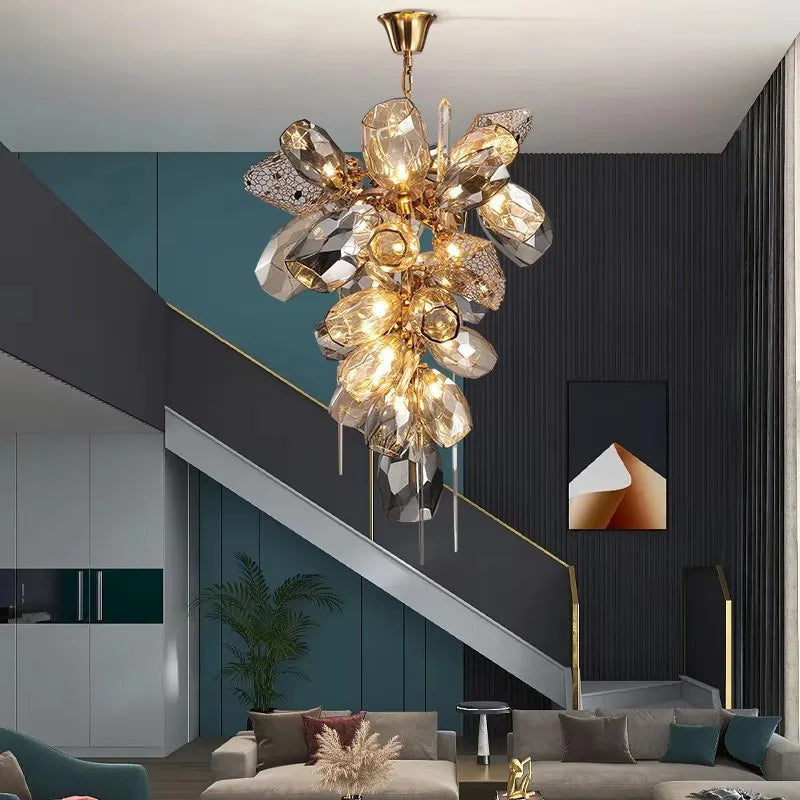 A gold chandelier with cascading faceted crystals hangs in a modern living room setting with a staircase.