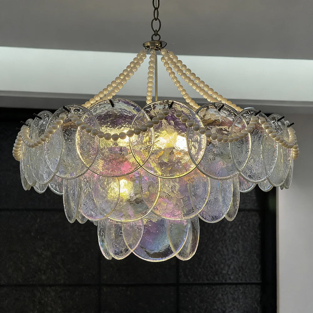 Close-up of a tiered glass chandelier with pearl bead strands and iridescent glass discs illuminated by warm light.