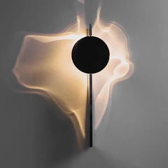 A single black circular disc mounted on a wall, illuminated to create abstract light shapes.