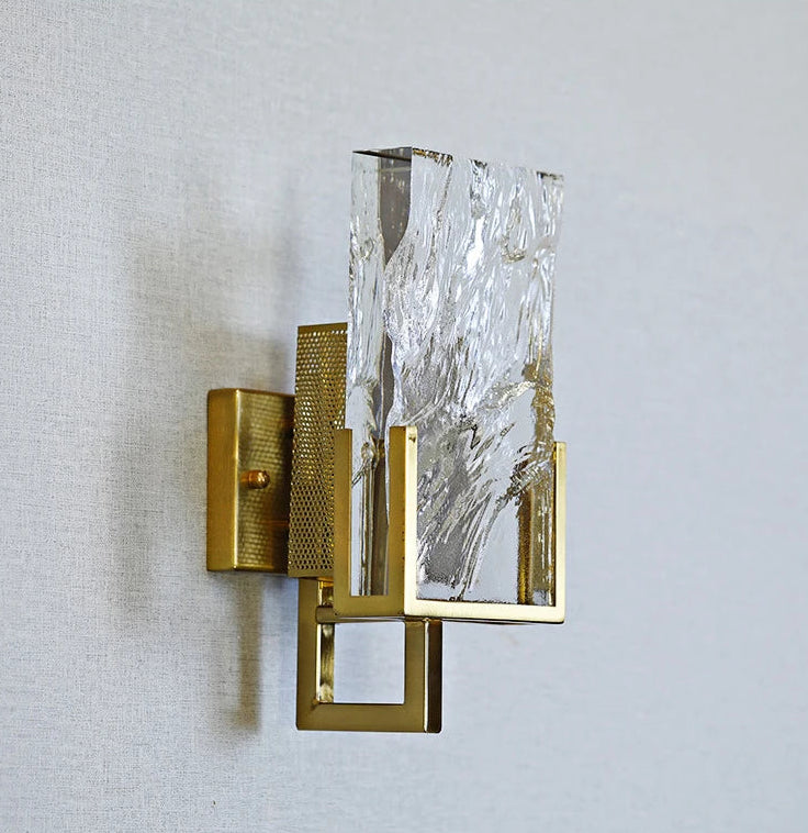 Wall sconce with gold finish and textured glass on a light gray background