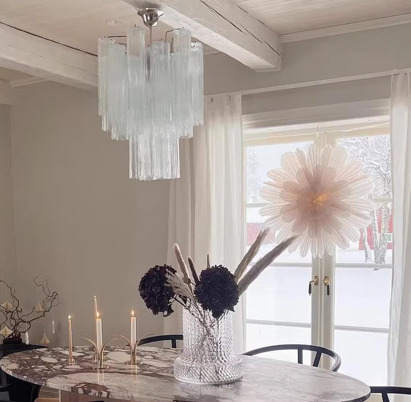 Dining room with marble table, chandelier, and large flower arrangement.