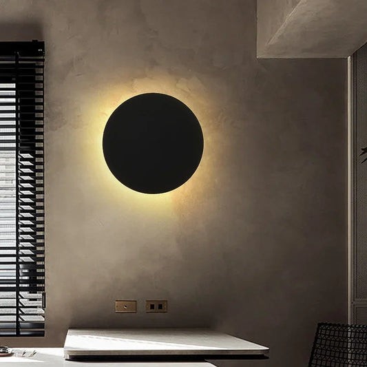 A single black circular wall sconce mounted on a textured wall, casting a warm glow.