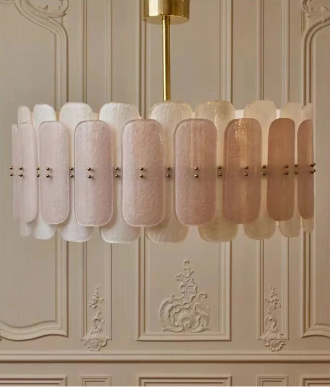 Decorative chandelier with pink and gold design on a wall with decorative molding.