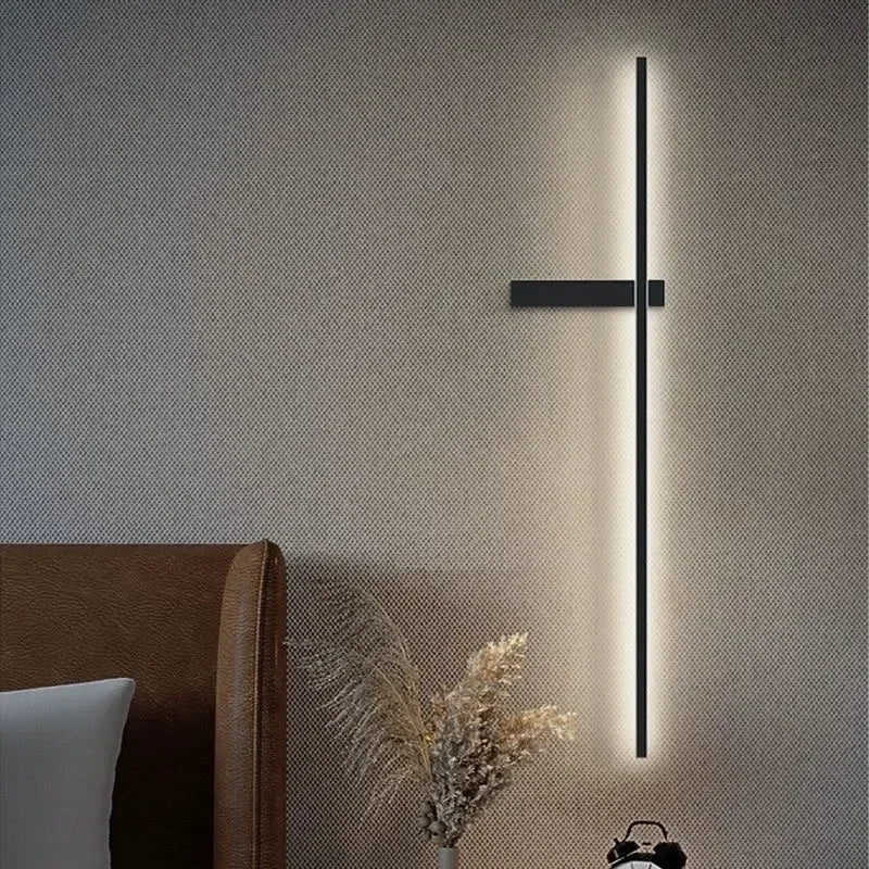 A black minimalist LED strip wall sconce mounted on a textured wall, casting a warm glow.