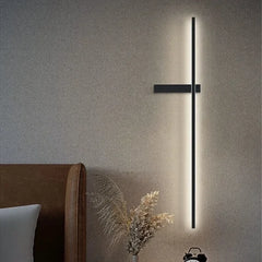 A black minimalist LED strip wall sconce mounted on a textured wall, casting a warm glow.
