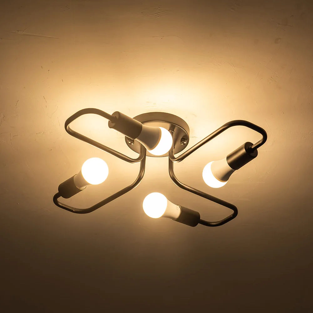 Black metal starburst semi-flush ceiling light fixture with four lit LED bulbs against a dark ceiling