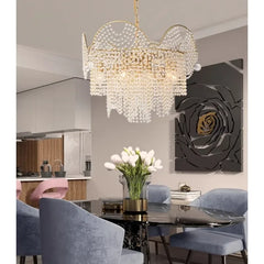 A dining room setting with a dark marble table and blue upholstered chairs, illuminated by a gold cascading crystal chandelier.
