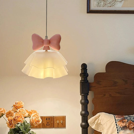 Pink bow tiered chandelier hanging above a bed, with bedside flowers and a lamp.
