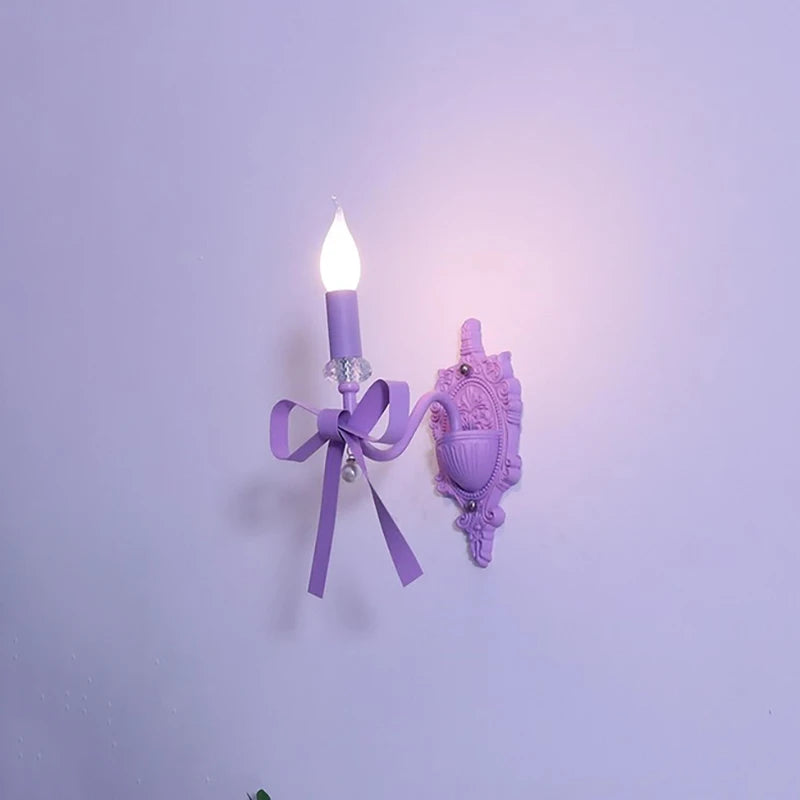 A single purple bow candle-style wall sconce with decorative accents, illuminated against a plain purple wall.