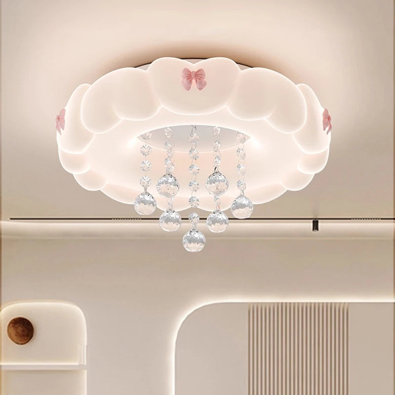 Close-up view of a white cloud-shaped ceiling light featuring pink bows and clear crystal accents, showing soft diffused lighting.