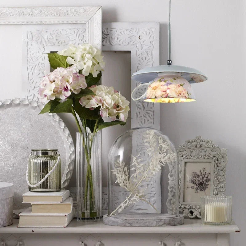 A floral ceramic pendant light illuminating a shelf decorated with flowers and books.