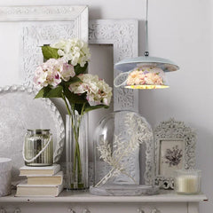 A floral ceramic pendant light illuminating a shelf decorated with flowers and books.