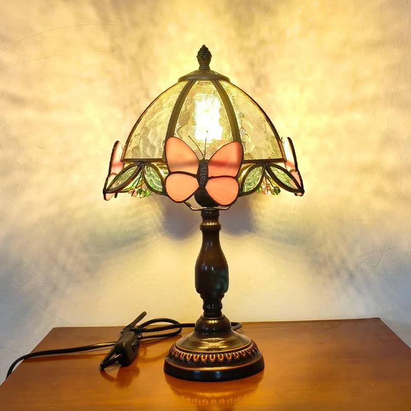 Decorative table lamp with stained glass shade featuring a butterfly design on a wooden surface.
