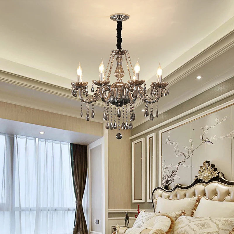 A smoke gray crystal chandelier installed in a bedroom, featuring multiple arms and sparkling crystal details, above a bed.