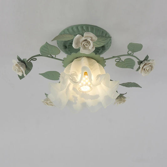 Close-up view of a green floral flush mount ceiling light with white roses and a ruffled glass shade with a visible E27 bulb socket.
