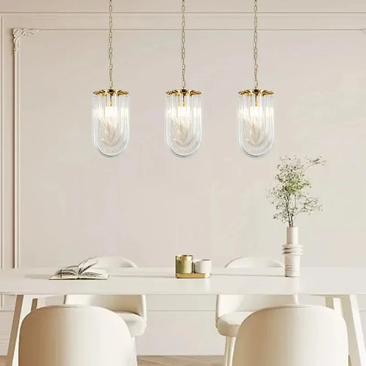 Three gold U-shaped pendant lights with clear glass tubes hanging over a white dining table with white chairs.