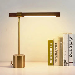 Brass and wood LED desk lamp with the light on, positioned next to a stack of books.
