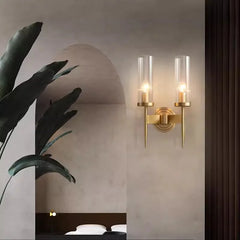 Gold wall sconce with two clear glass shades on a neutral wall.