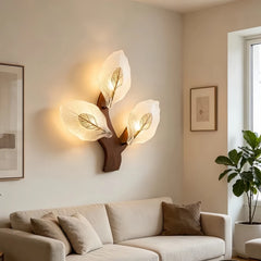 Wood leaf wall sconce with three frosted glass shades shaped like leaves, mounted on a wooden base against a cream wall above a sofa.
