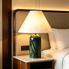 Green stone art ceramic table lamp with a fabric shade, placed on a nightstand next to a bed.