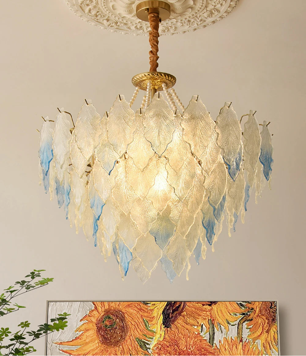 Decorative chandelier with feather-like design on a ceiling, with a sunflower painting in the background.