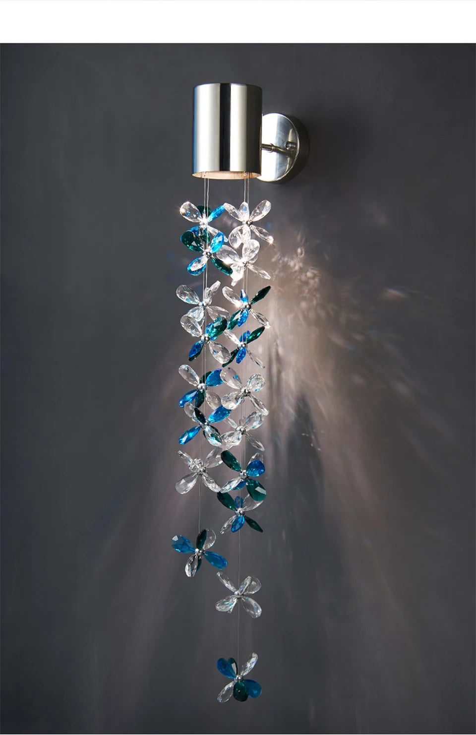 Polished chrome wall sconce featuring a hanging chain of blue and clear crystal flowers, creating a cascading effect with light.