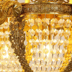 Close-up of the gold chandelier's crystal strands and decorative metalwork, with blurred lights in the background.