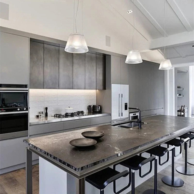 Three clear pleated glass drum pendant lights hanging above a kitchen island.