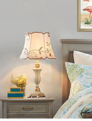 Ornate table lamp with a teal and gold resin base placed on a bedside table next to a framed picture.