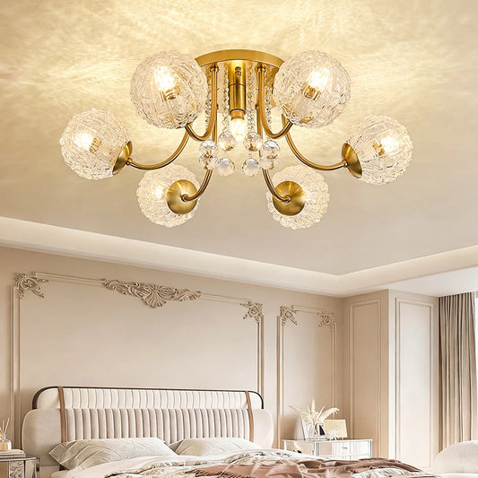 Close-up of a polished gold semi-flush ceiling light with ripple glass globes and crystal accents, mounted on a bedroom ceiling above a bed.
