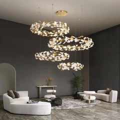 A grand interior space featuring a tall cascading chandelier with multiple gold leaf rings, complemented by modern furniture.