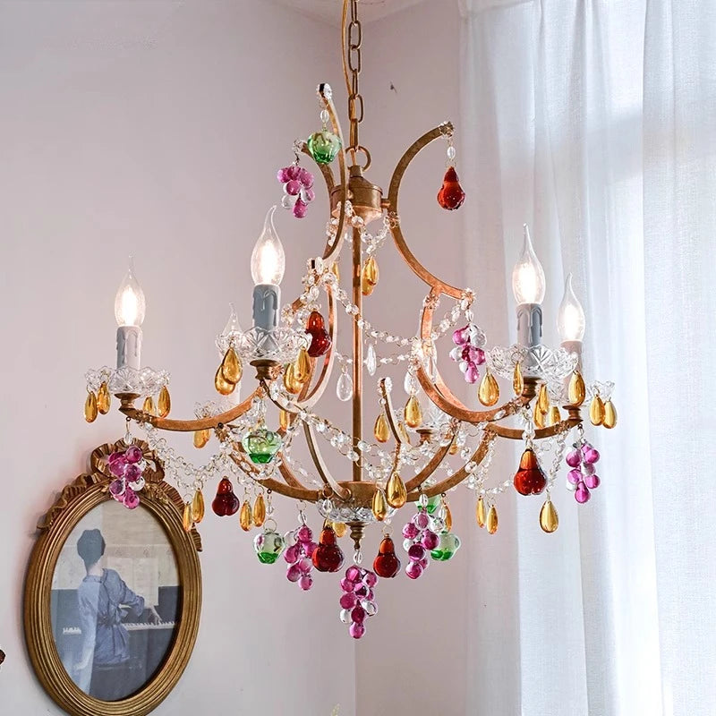 A gold chandelier with colorful crystal accents, resembling flowers and grapes, hangs from a ceiling.