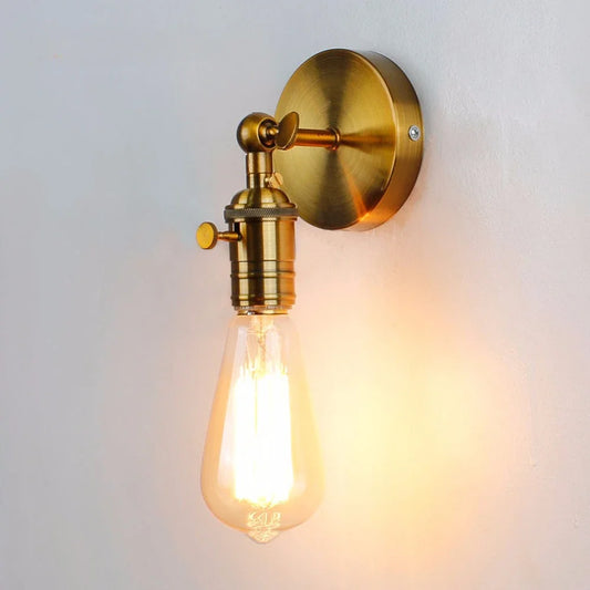 Gold industrial-style wall sconce with an adjustable folding arm and exposed Edison-style bulb mounted on a white wall.