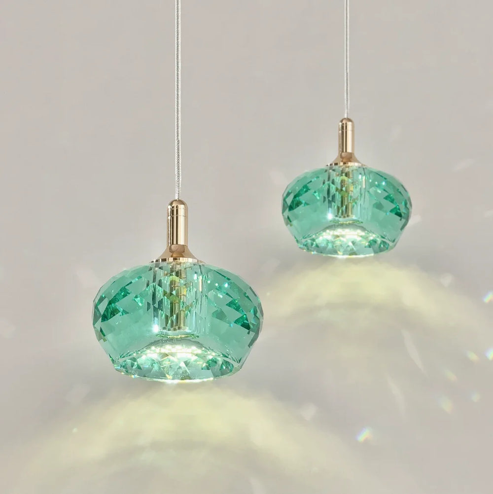 Two green faceted crystal pendant lights with gold accents hanging against a white background, casting light patterns.