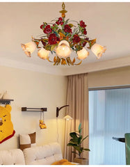 A wider shot of a gold floral chandelier with red rose buds, installed in a room with neutral-toned walls and furniture.