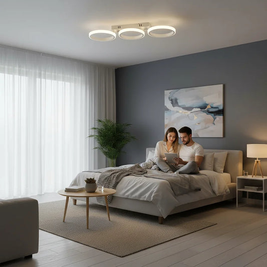 Couple sitting on a bed in a modern bedroom, illuminated by a white LED ceiling light with three rings.