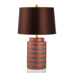 An orange ceramic table lamp with a navy and white geometric pattern and a brown fabric shade against a white background.