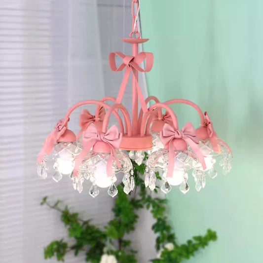 Front view of a pink multi-arm chandelier featuring pink bows, crystal pendants, and clear glass shades, with greenery in the background.